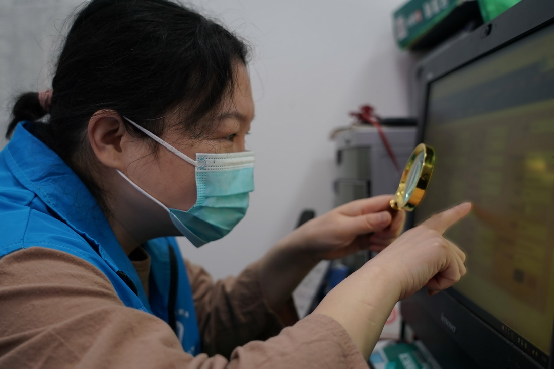 在北京市海淀区八里庄街道首师大社区居委会,马尔东手握放大镜进行疫情防控信息统计工作(5月13日摄)。新华社记者 任超 摄