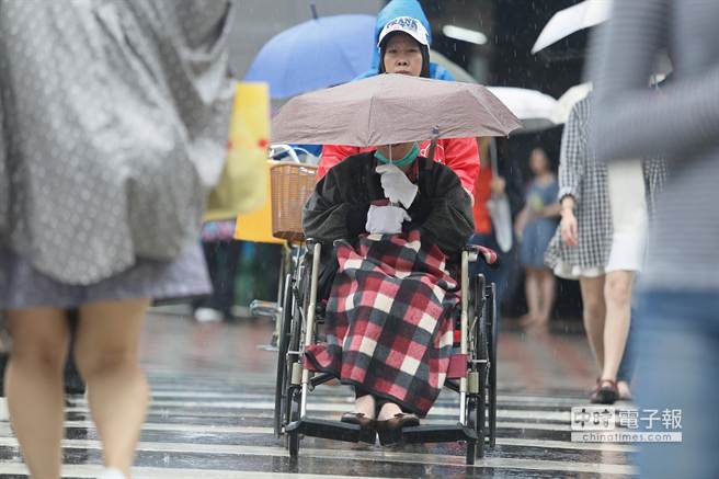 台湾中部以北从中午开始雨势增大，连坐轮椅外出的民众都撑起伞具避雨。(中时电子报图张铠乙摄)